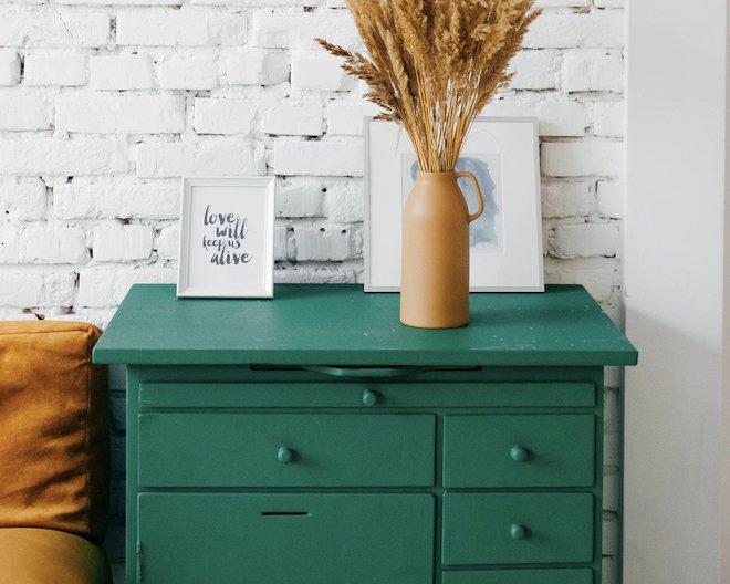 a green chest of drawers and on top of it , there are two frames and a vase